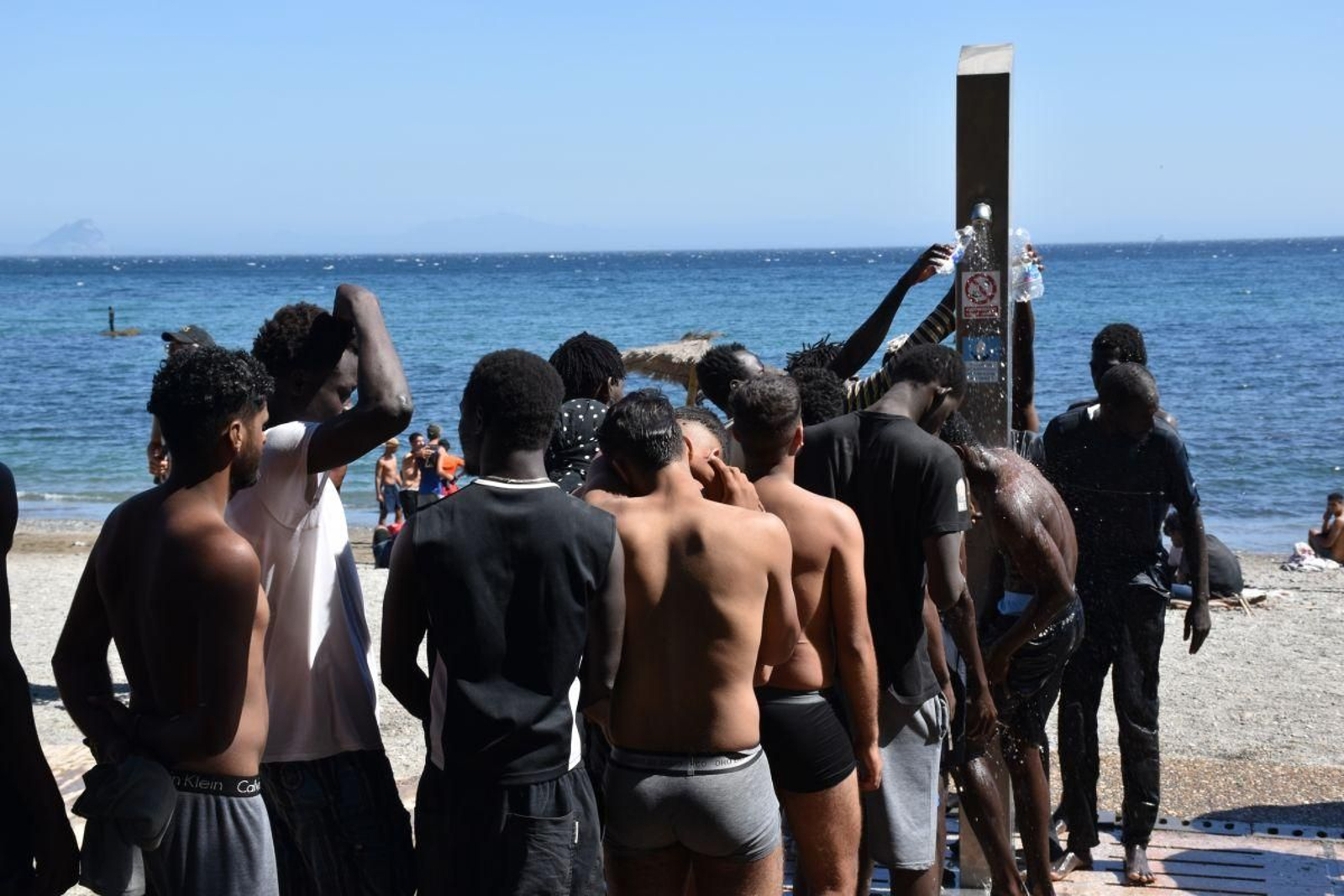 Varias personas se asean en las duchas públicas, en la playa del Trampolín.
