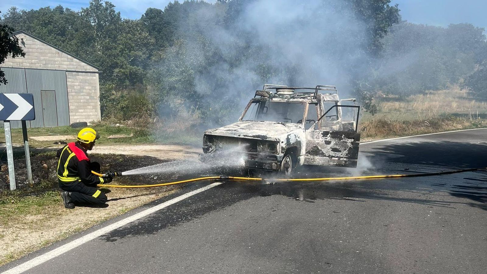 Un bombero se emplea en acabar con las llamas que salen del coche.