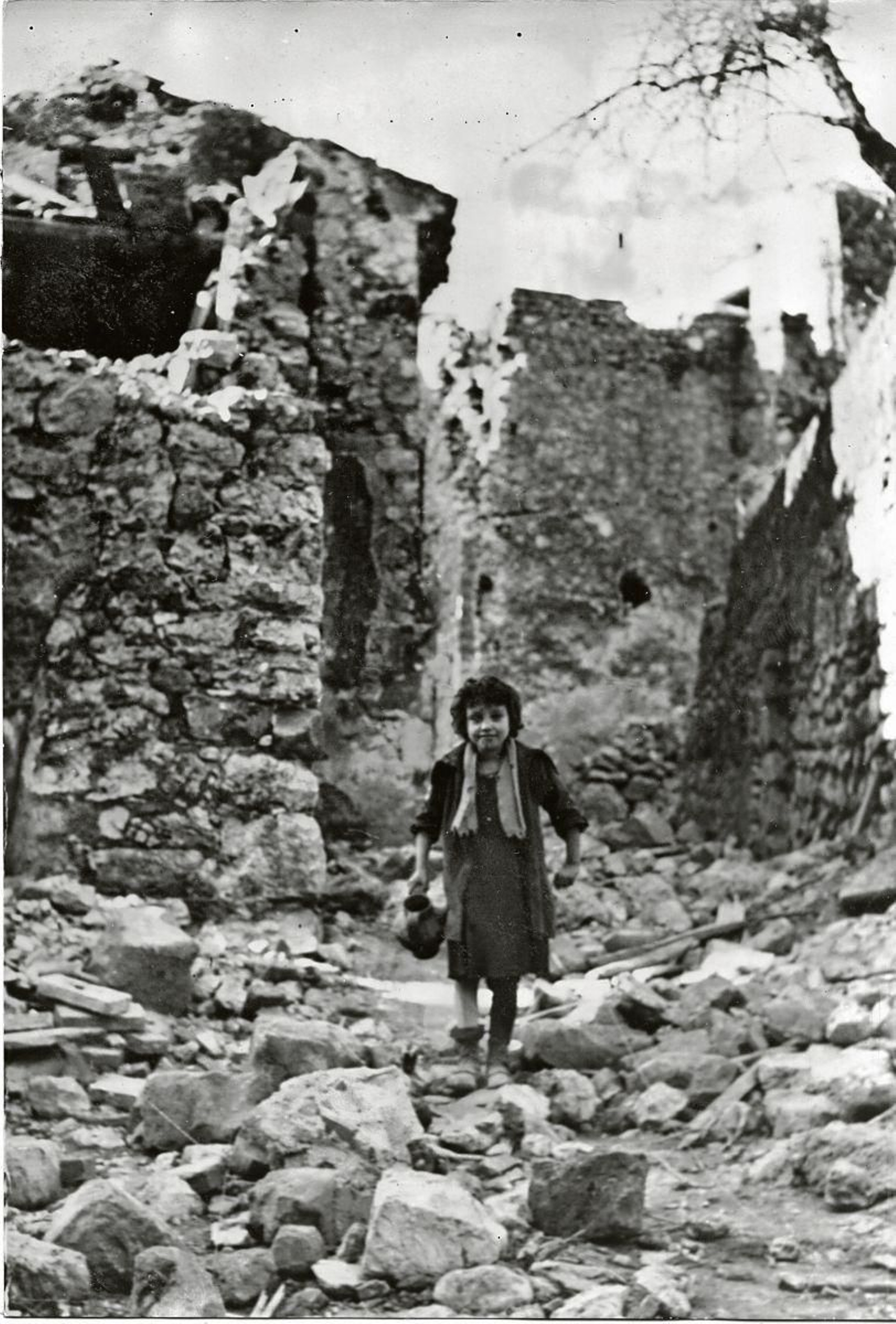 Niña italiana buscando agua entre las ruinas.