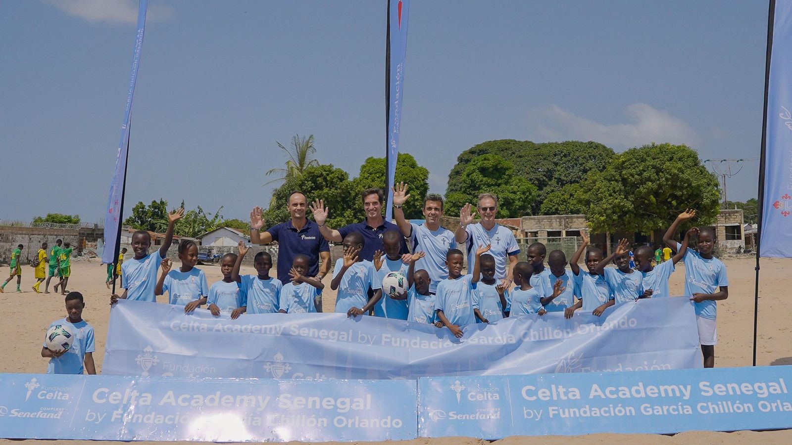 Uno de los equipos de niños saluda a la cámara sobre el campo de juego, de tierra.