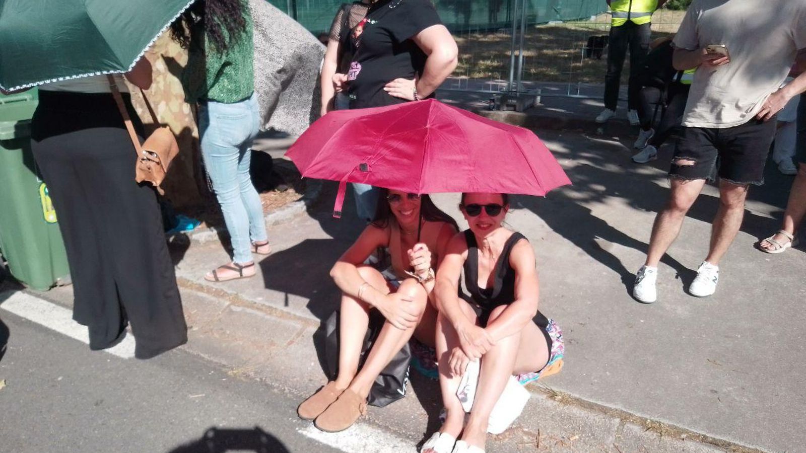 Dos fans se protegen del sol a la cola con un paraguas.