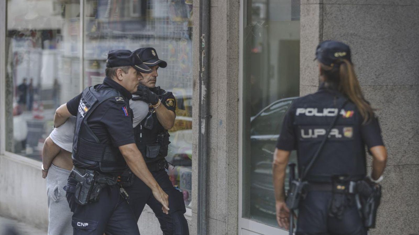 El detenido entra a su vivienda para el registro custodiado por agentes de la Policía Nacional.