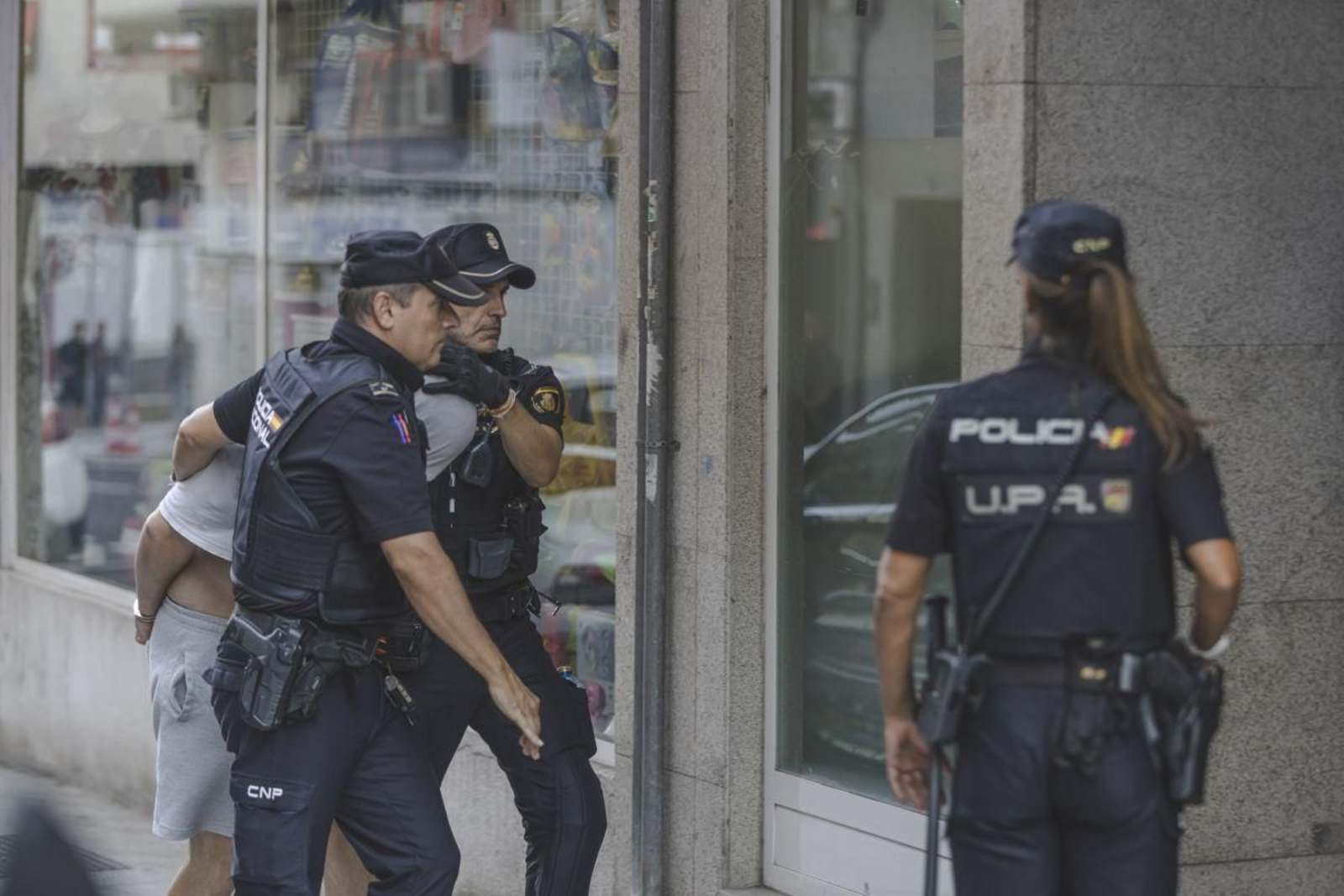 El detenido entra a su vivienda para el registro custodiado por agentes de la Policía Nacional.