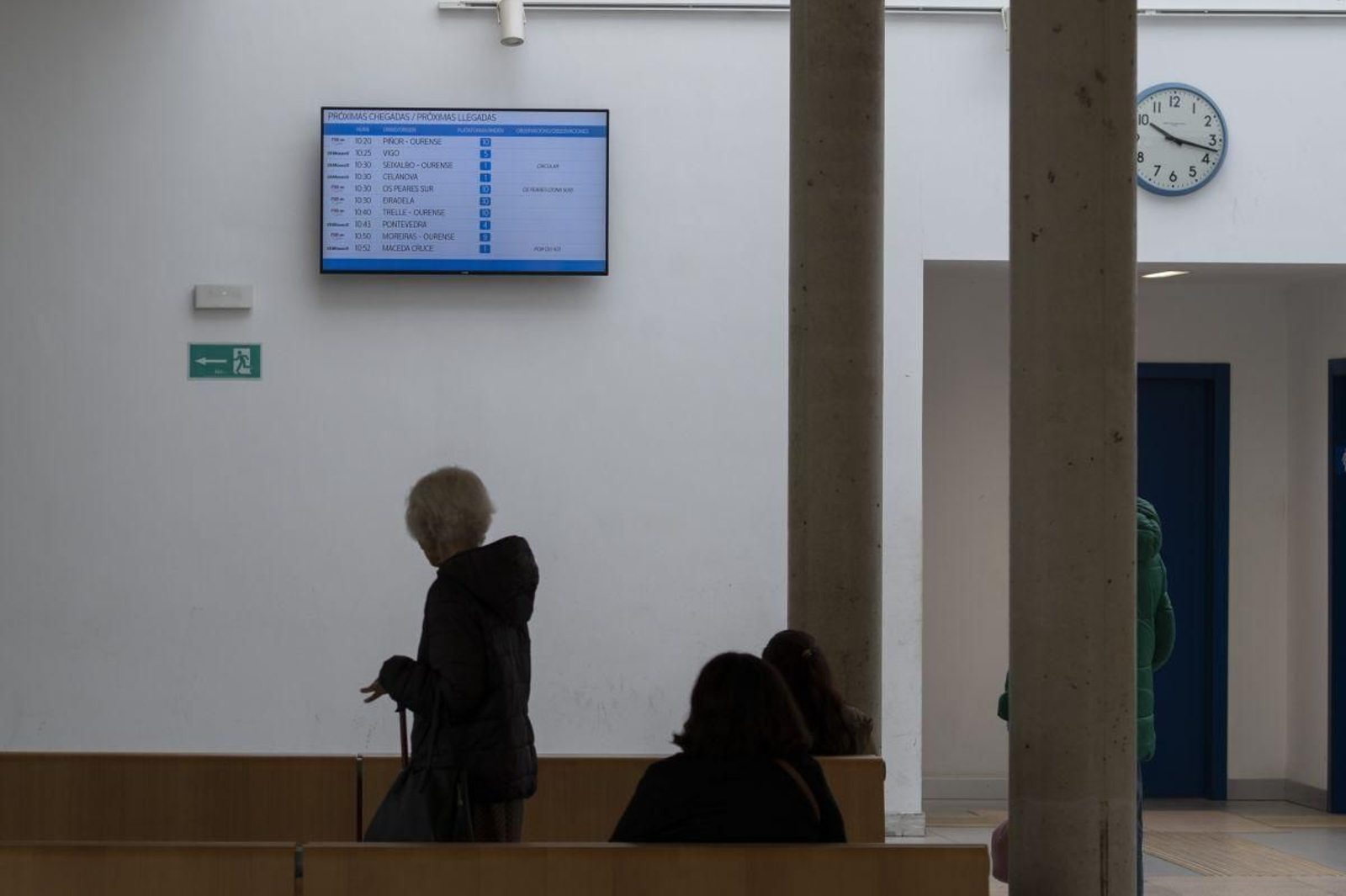 Viajeros esperando en la estación de autobuses de Ourense observan la pantalla de llegadas y salidas