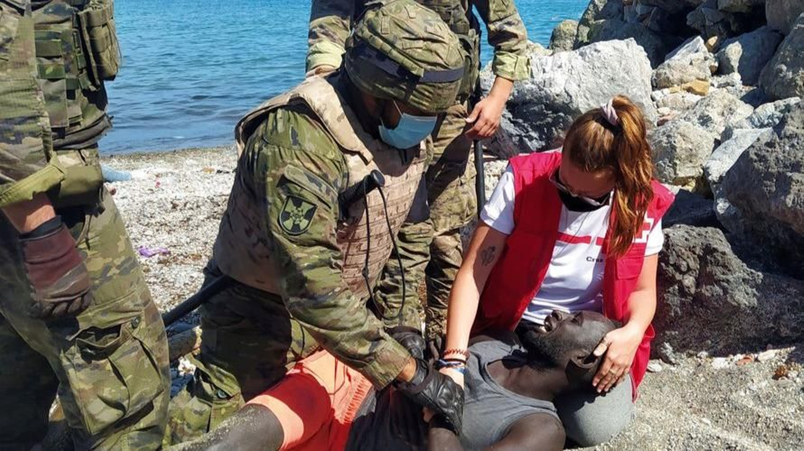 Un militar y una colaboradora de Cruz Roja atienden a un inmigrante en la playa.