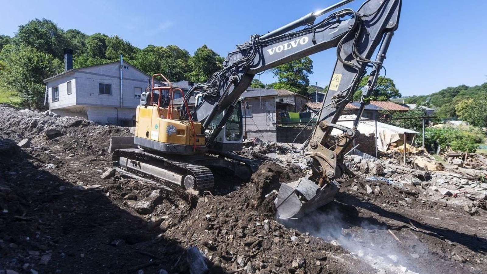 Una excavadora trabajando en los escombros de la aldea de A Bouza.
