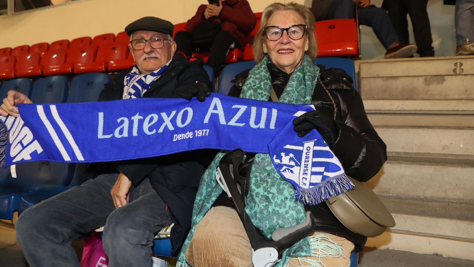 Una pareja de aficionados con su bufanda, listos para el inicio del partido.