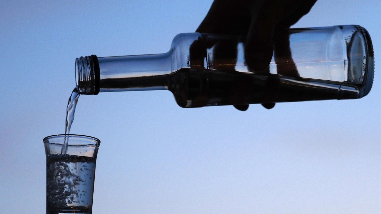 Un hombre vierte licor de una botella pequeña en un vaso.