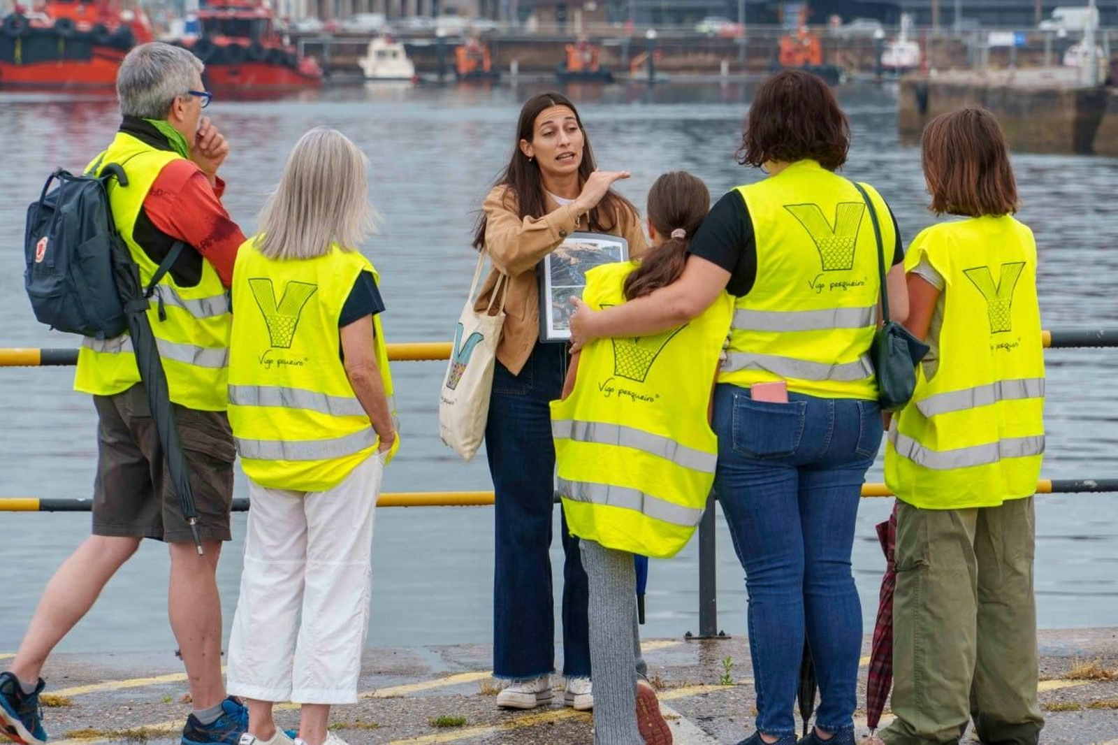 Grupo de visitantes en el Puerto de Vigo atendiendo a la explicación de Lourdes Porto, guía de la actividad.