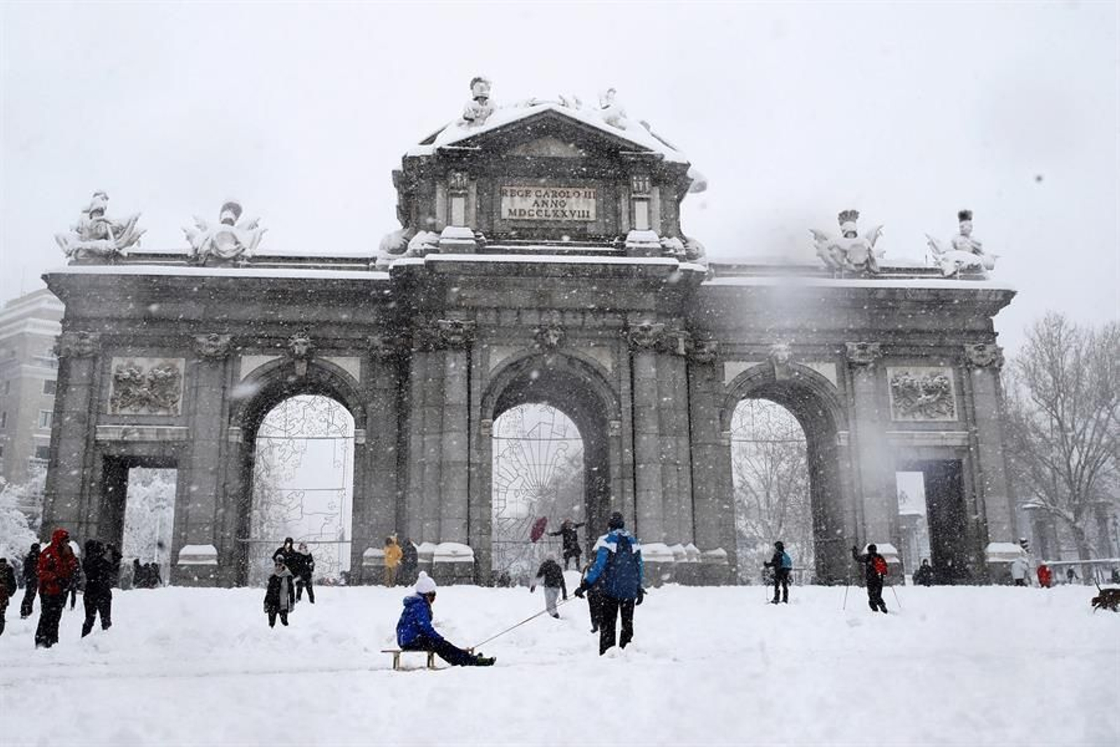 Varias personas caminan junto a la Puerta de Alcalá de Madrid, este sábado