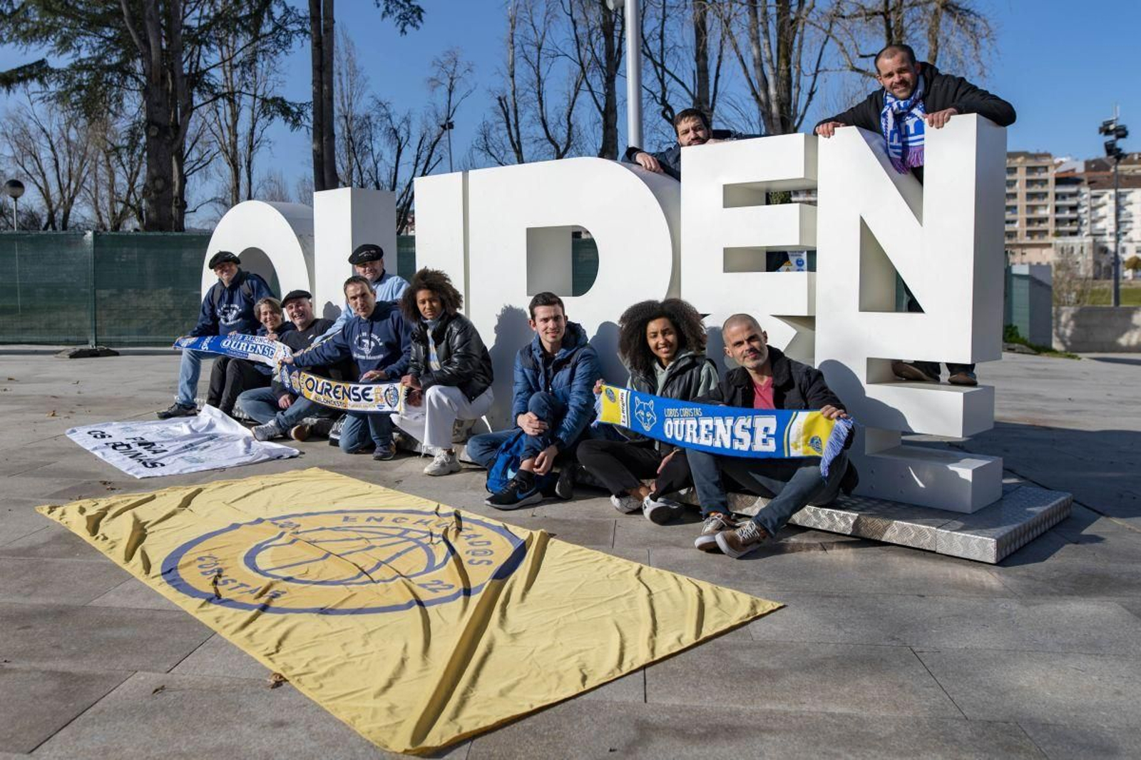 Representantes de las peñas Os Boinas y Enchufad@s, posan en el cartel de la ciudad.
