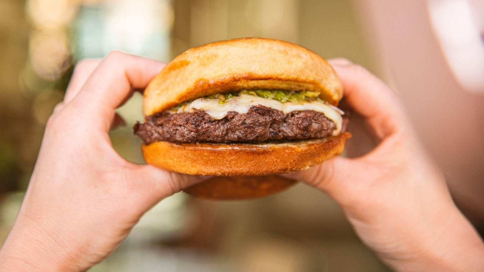 Una persona ingiriendo una hamburguesa.