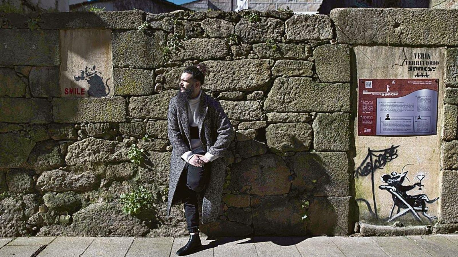 El artista verinés Álex Araújo posa con obras de Banksy reproducidas en la villa. Foto: Martiño Pinal.
