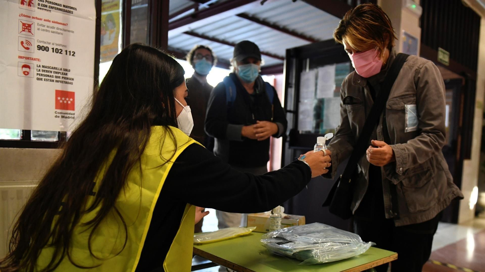 Una mujer ofrece gel hidroalcohólico a los votantes que acceden al colegio Roma de Madrid durante la jornada electoral