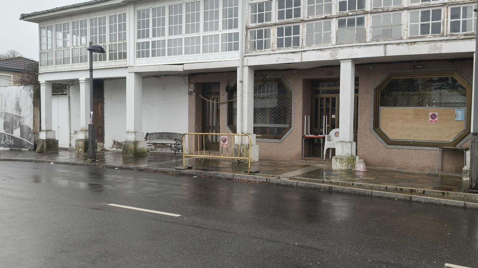 Vallas con la señal de prohibido aparcar y señales en los comercios en la OU-1005 a su paso por el centro de Riós.