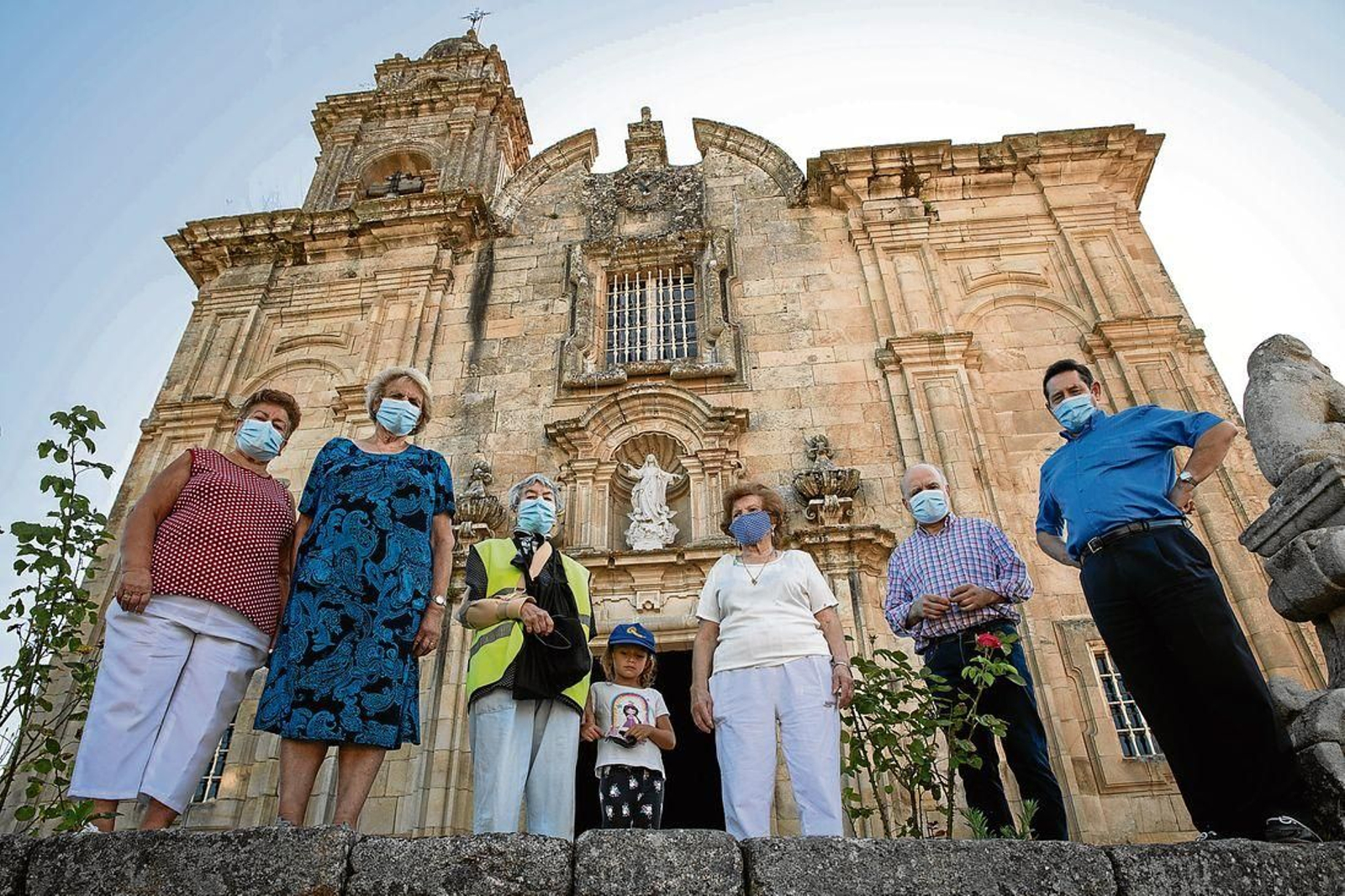 Luisa Álvarez, Paz Pato, Fina Álvarez, Hannah Vázquez, Carmen Blanco, Santiago Notario y Francisco Enríquez posan delante de la iglesia parroquial de Santa María de Melias, en Pereiro de Aguiar. (Foto: Óscar Pinal)