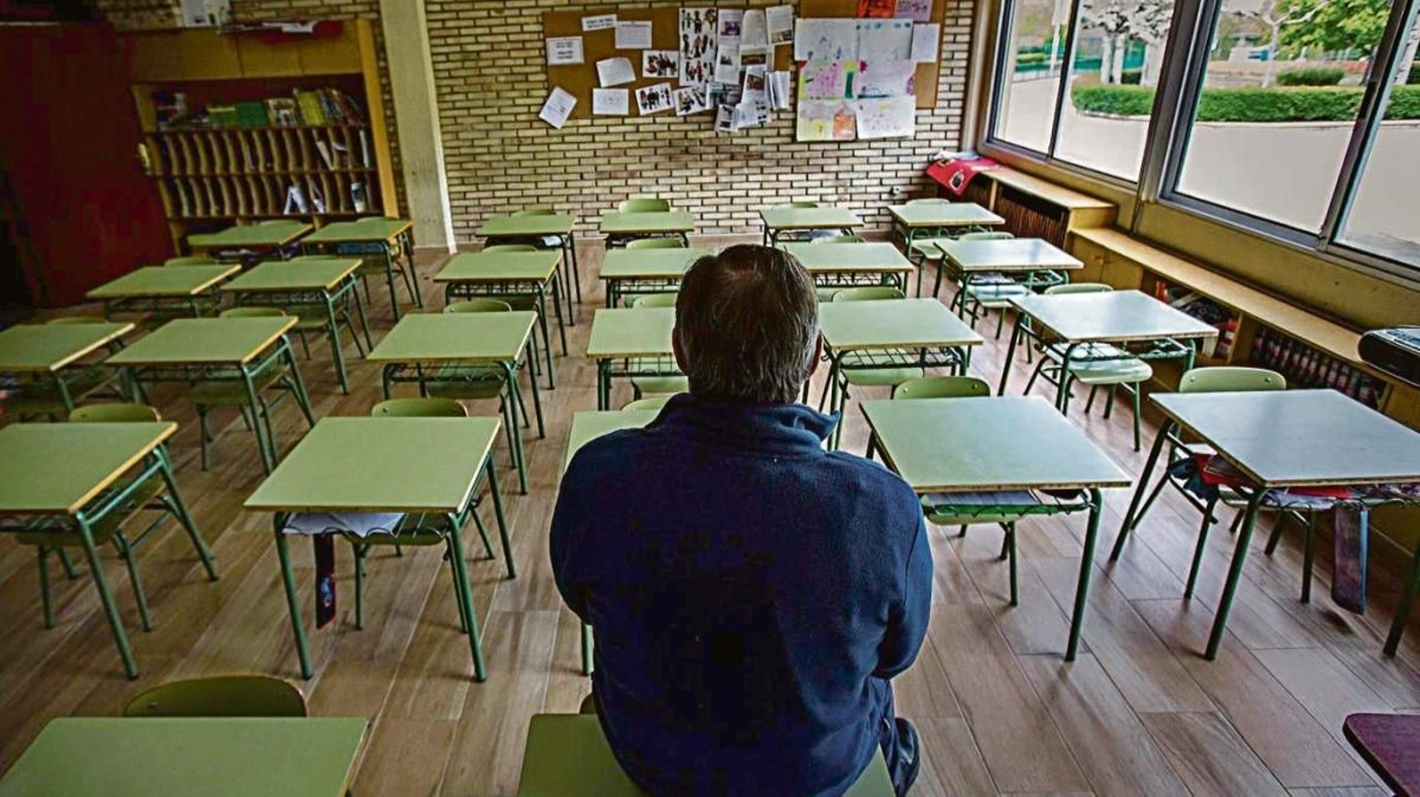 Un profesor, sentado en su mesa en una clase vacía.