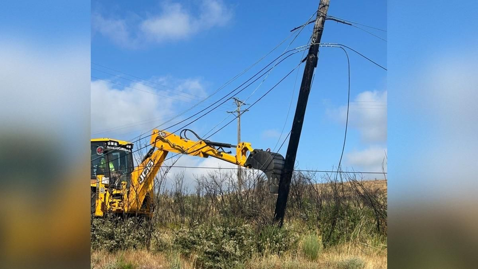 Un operario retira con una máquina un poste de teléfono calcinado en Cualedro.