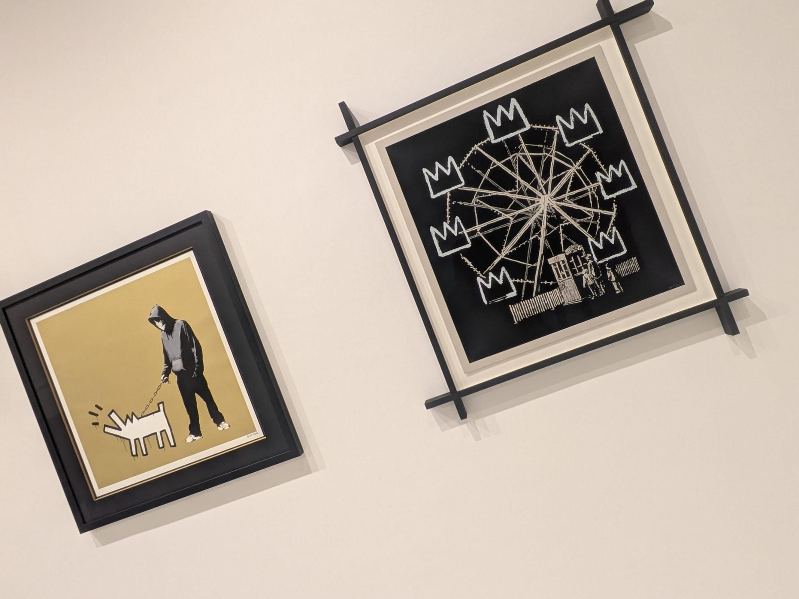 A la izquierda, una obra titulada "Choose Your Weapon" del artista Banksy, lanzada en 2010 y producida por Pictures on Walls, que muestra a una figura con capucha sosteniendo una cadena con un perro al estilo de Keith Haring. El cuadro de la derecha es una obra de arte titulada "Banksquiat" de Banksy, creada en 2019 como homenaje al artista Jean-Michel Basquiat. La obra representa una noria cuyas cabinas son las famosas coronas de Basquiat, criticando la comercialización del arte callejero.