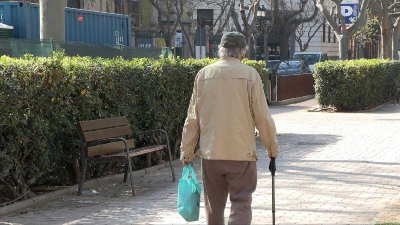 Una persona mayor con un bastón camina por un parque.