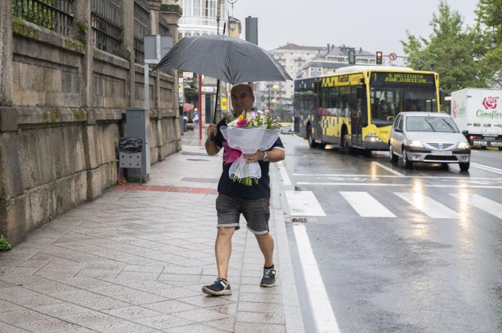 Un hombre se protege de la lluvia con un paraguas mientras que lleva en la mano un ramo de flores.