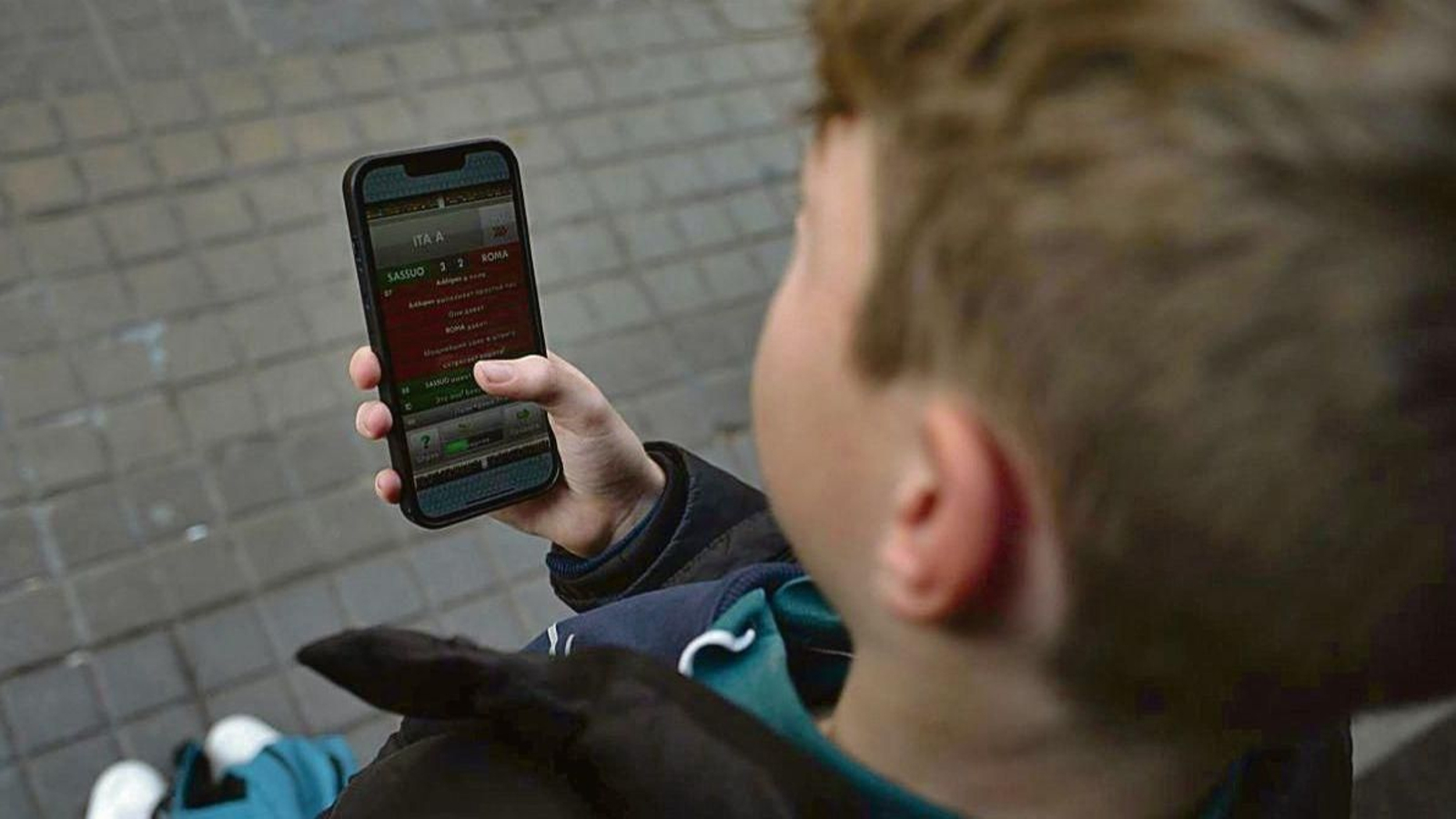 Un niño menor de edad, atento a la pantalla de un teléfono móvil.