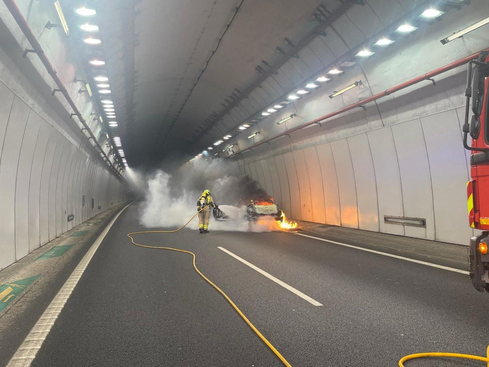 Bomberos apagando las llamas originadas en el motor del coche averiado.