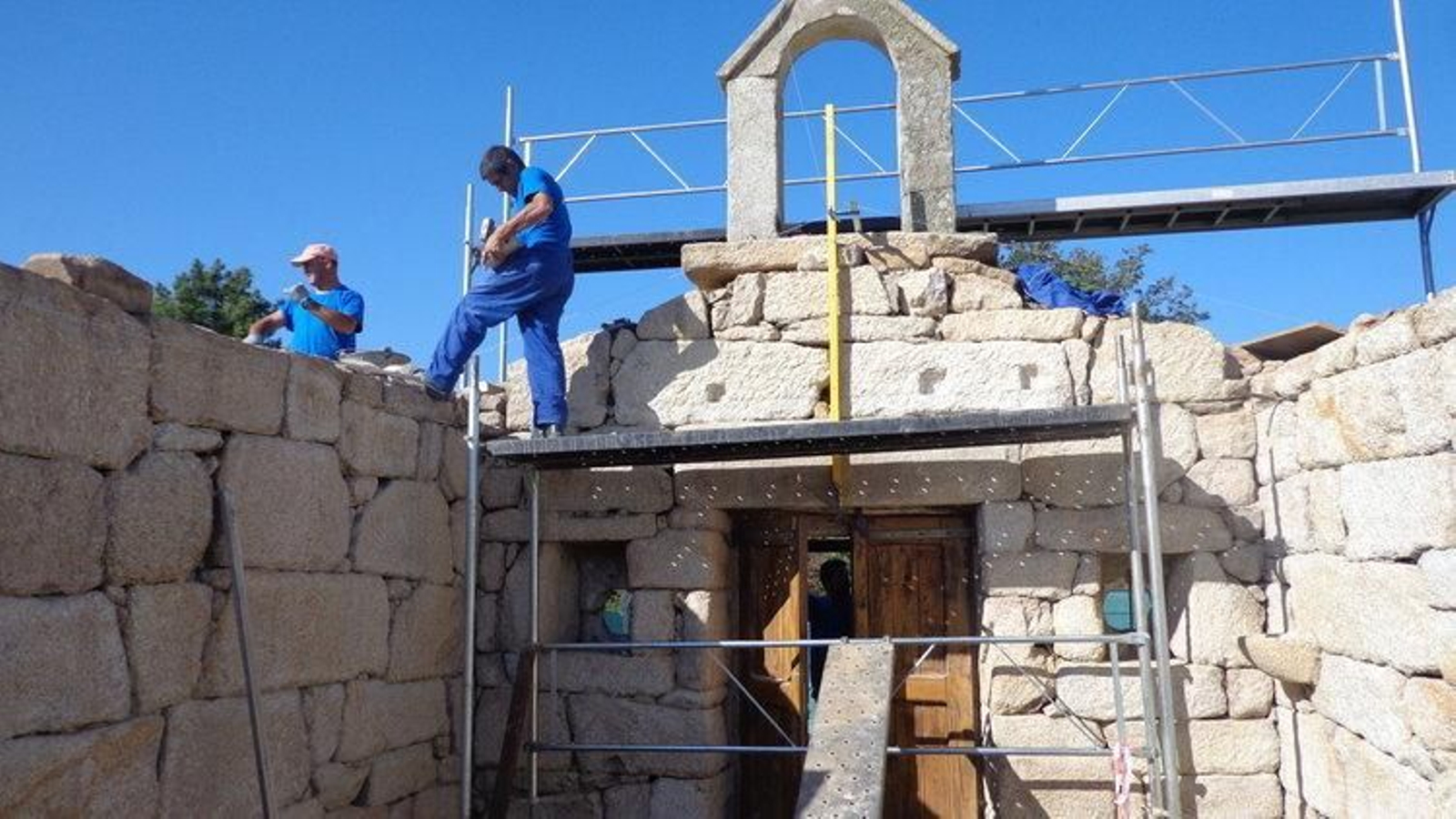 Dos operarios colocan piedras en una de las paredes cercanas al campanario del templo.