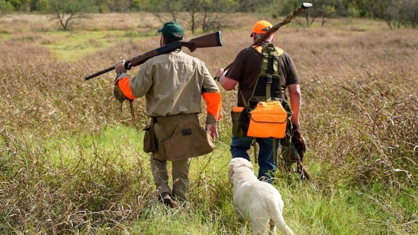 Dos cazadores pasean por un coto con su equipo de caza y acompañados de un perro.