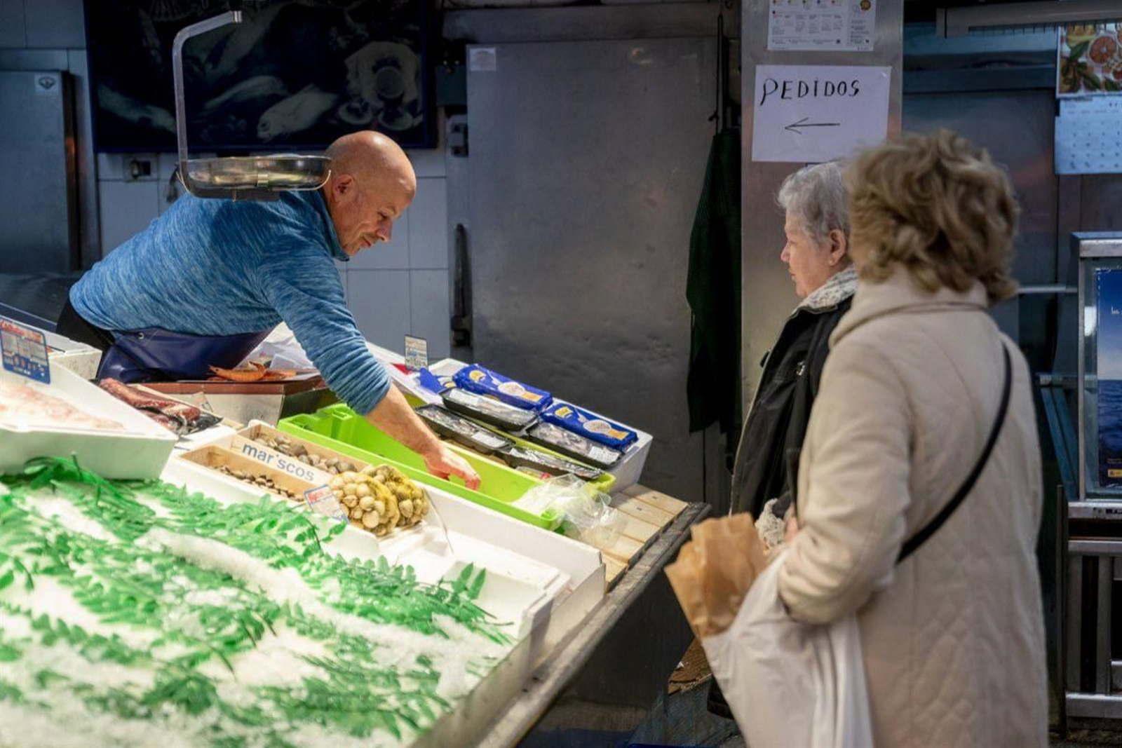 Dos mujeres observan el producto y los precios en una pescadería.