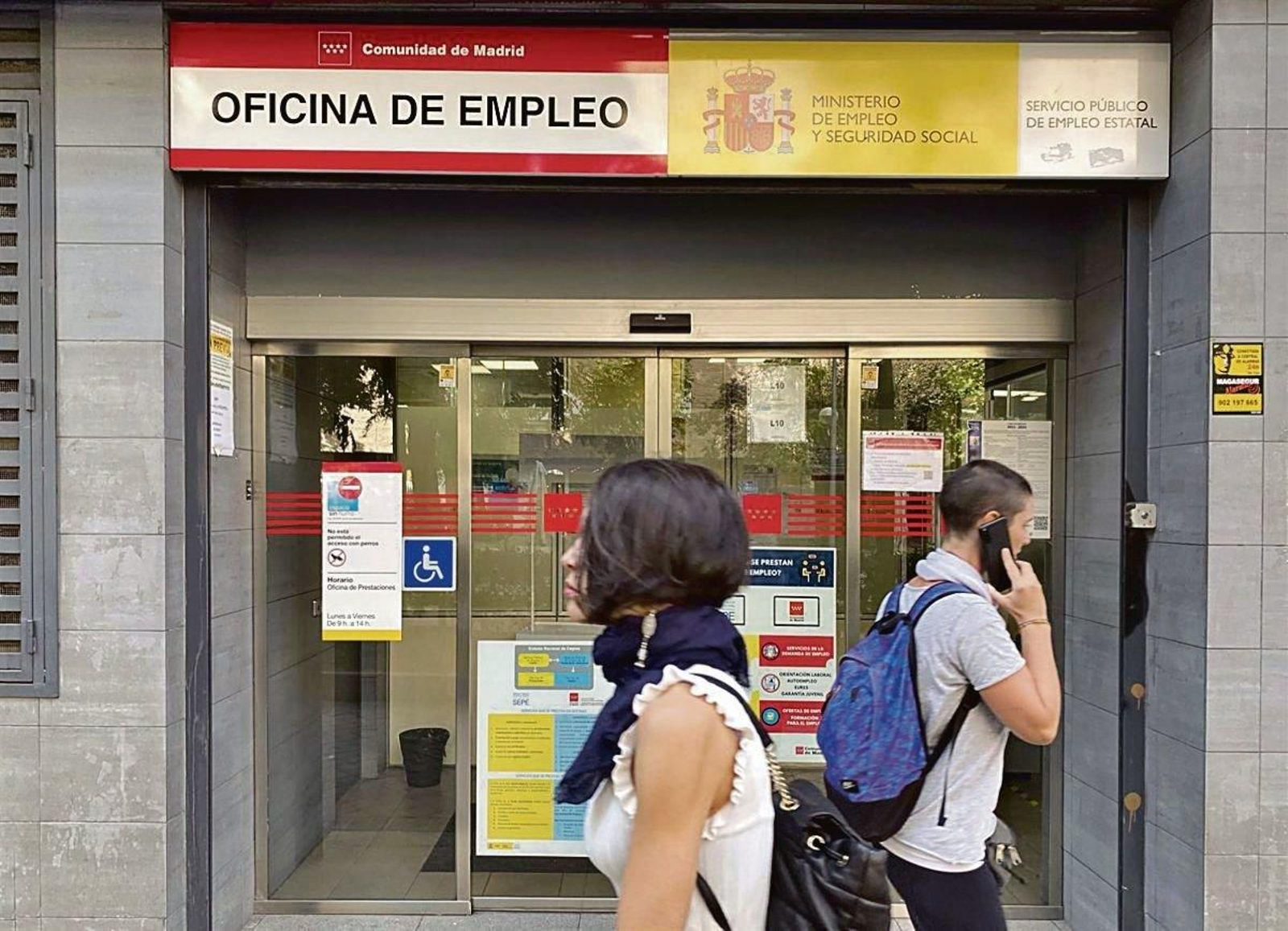 Dos jóvenes pasean por delante de una oficina de empleo.