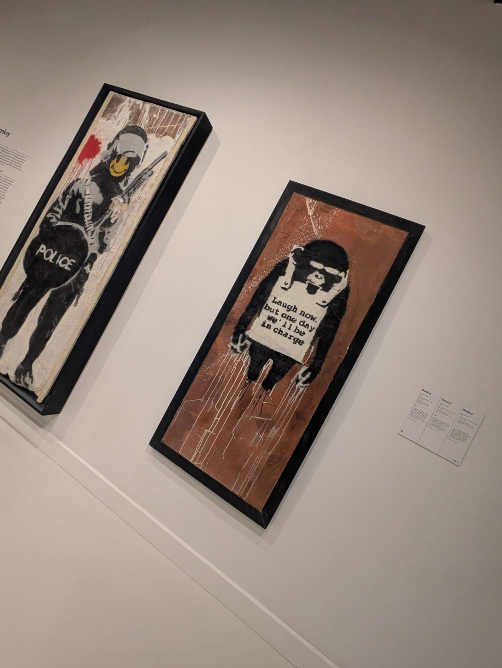 La imagen muestra una obra de arte titulada "Smiling Copper" del artista callejero Banksy, que satiriza a la autoridad policial, a la izquierda. Y a la derecha . La imagen muestra dos paneles de la obra Laugh Now (Ríe ahora) del artista Banksy, originalmente creados en 2002.