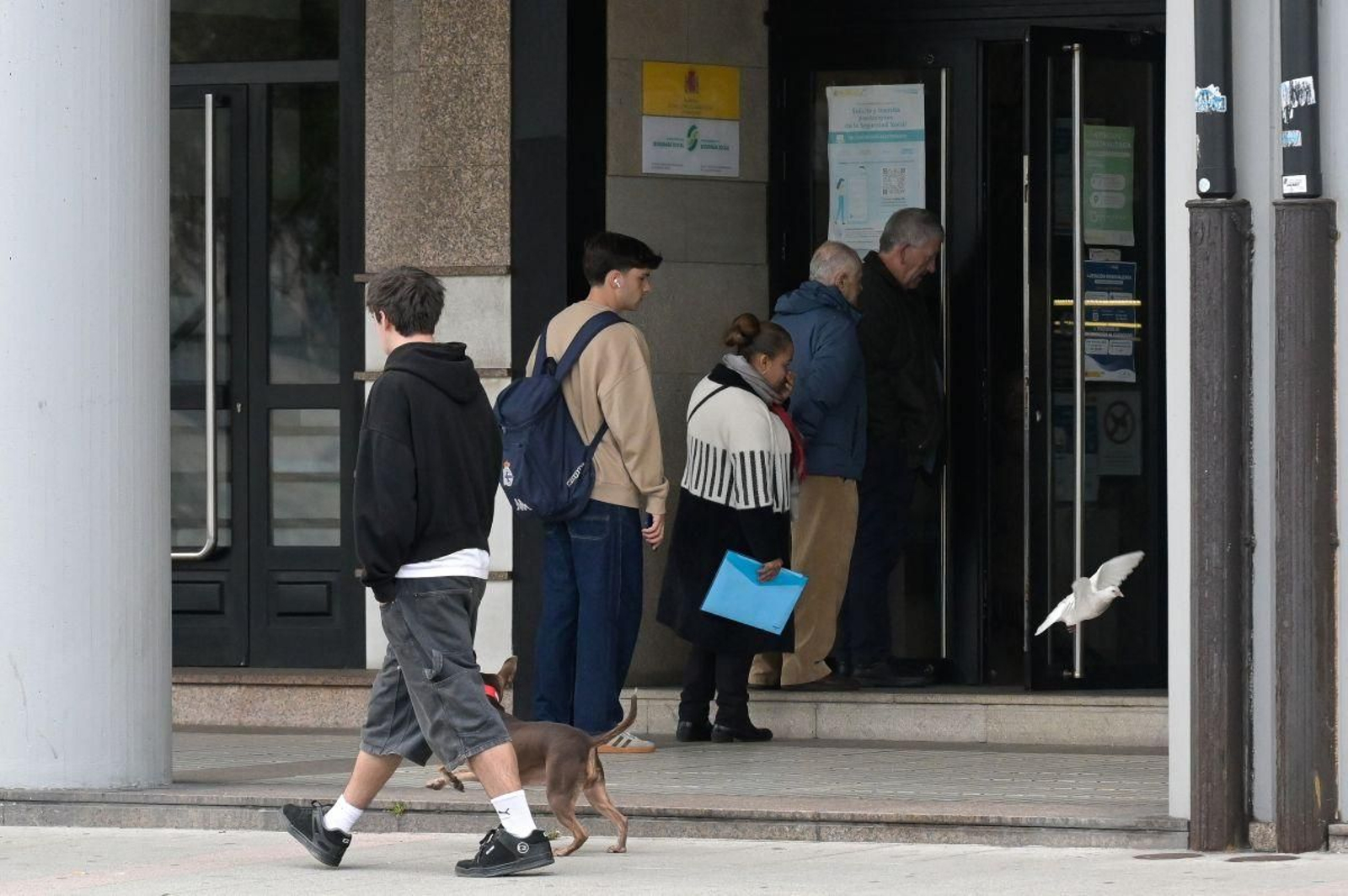 Varias personas hacen cola en una oficina del INSS en A Coruña por la regularización extraordinaria de migrantes.