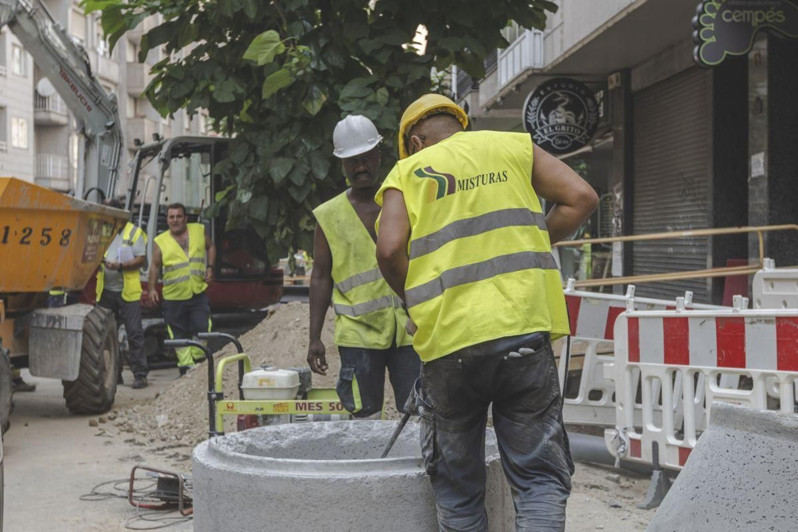 Los obreros trabajan delante de un negocio con la persiana cerrada.