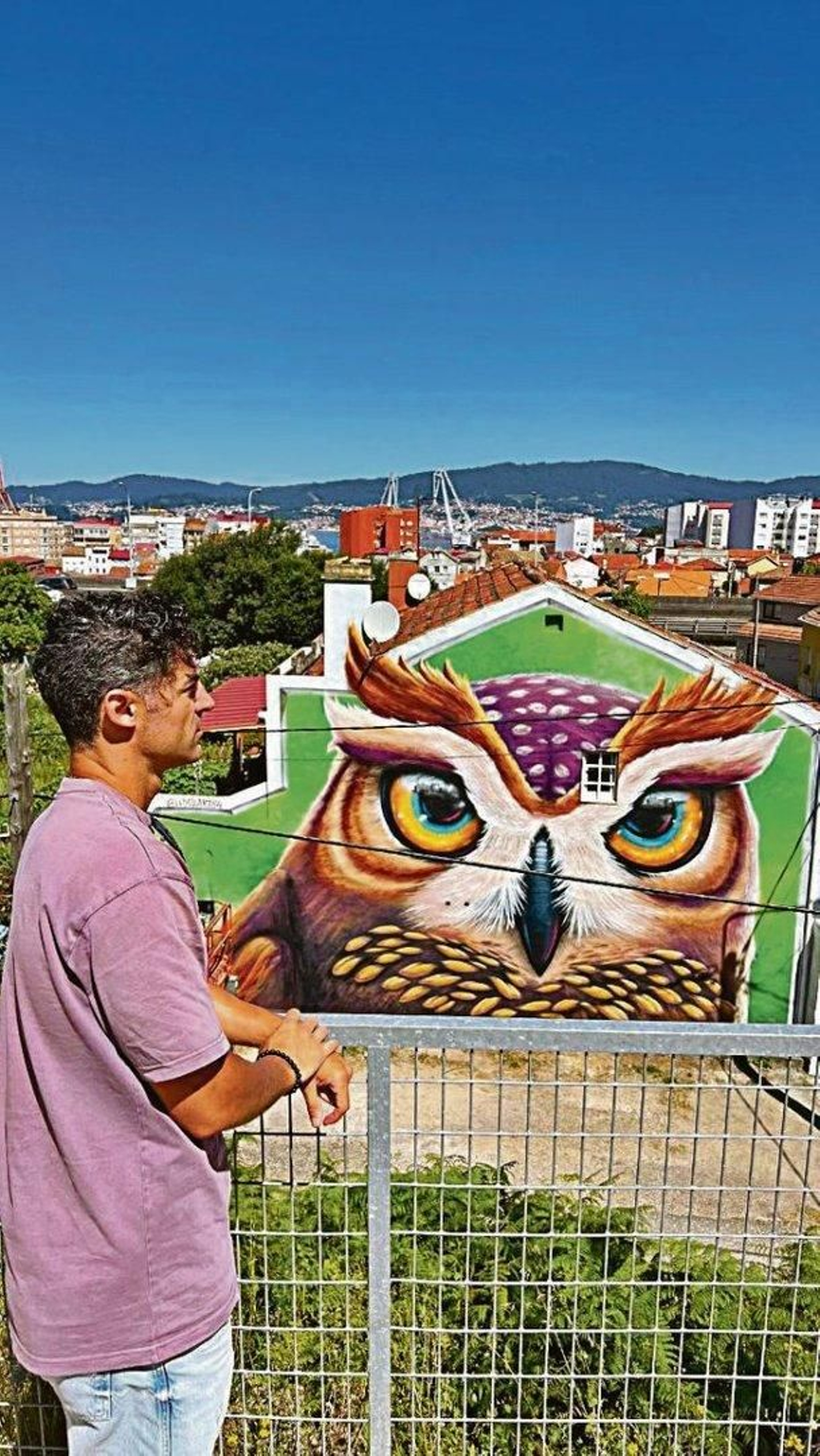 El artista vigués Pablo Loyola ante su mural “O moucho da vía” en la calle Robleda 118.