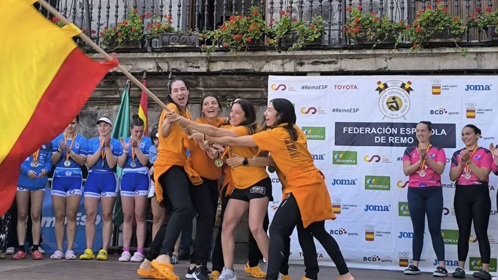 La tripulación chapeleira agita la bandera de campeonas en el podio de Castro Urdiales, en Cantabria.