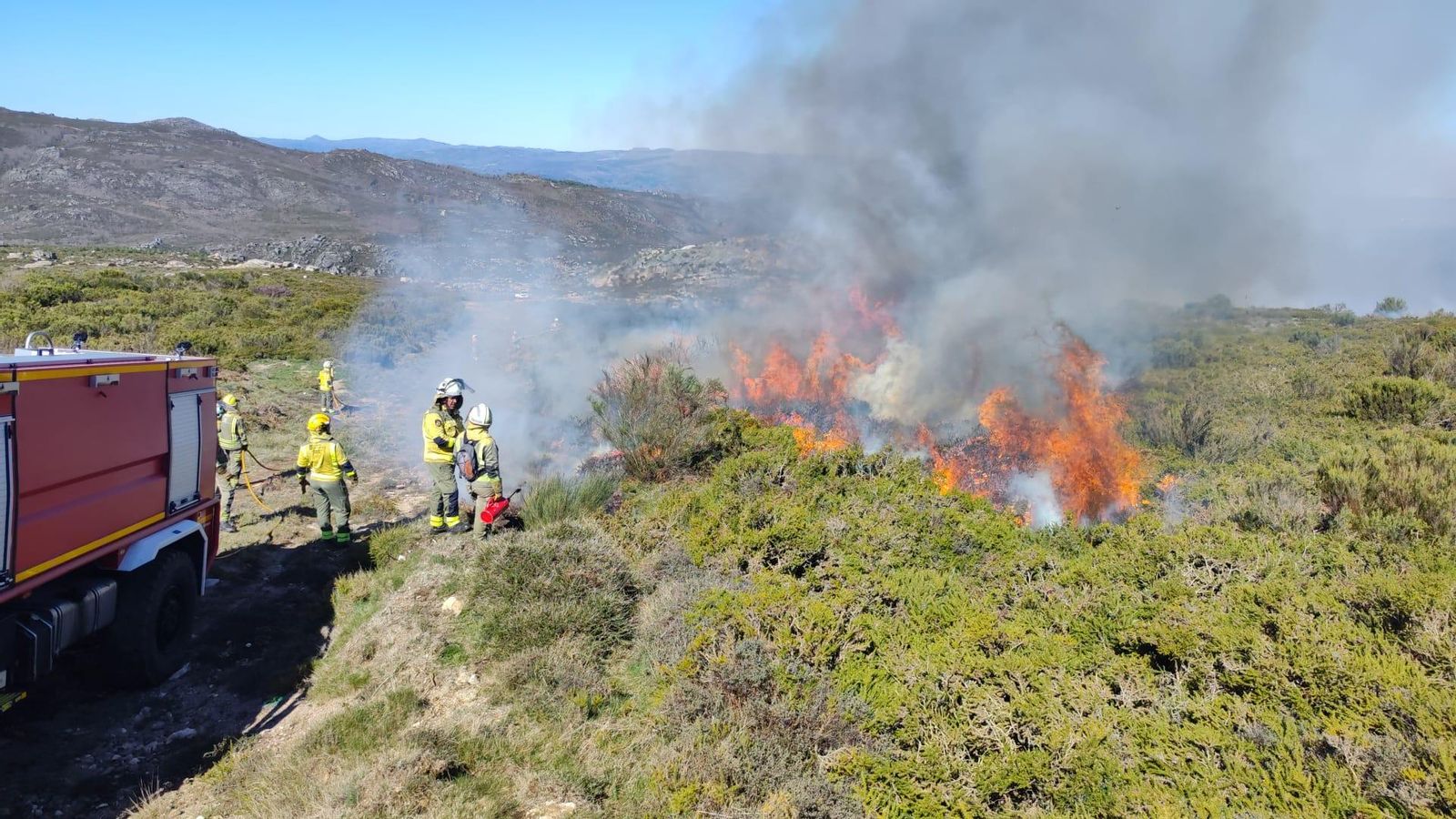 Bomberos combaten las llamas en los montes de Muiños mientras el humo se eleva sobre la zona.