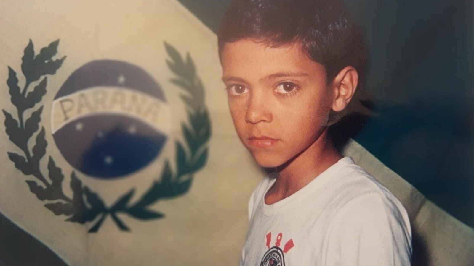 Roberto Norbiato durante su adolescencia, posando frente a la bandera del estado brasileño de Paraná.