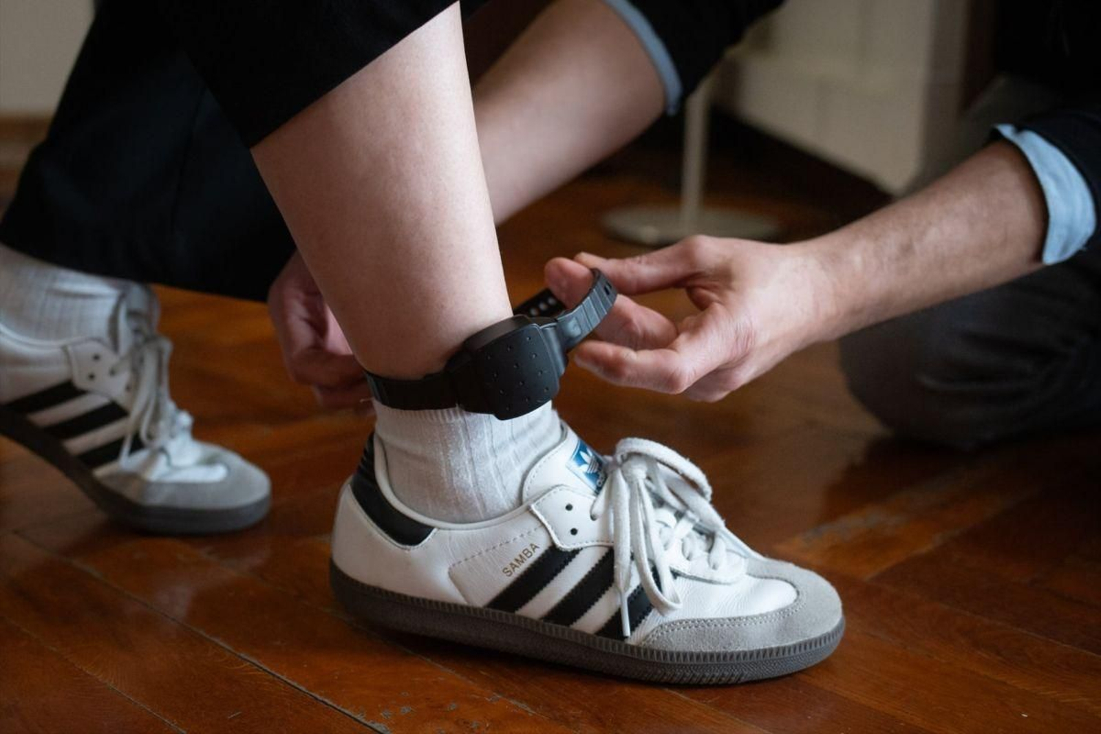 Una persona le coloca a otra una pulsera electrónica de geolocalización telemática.