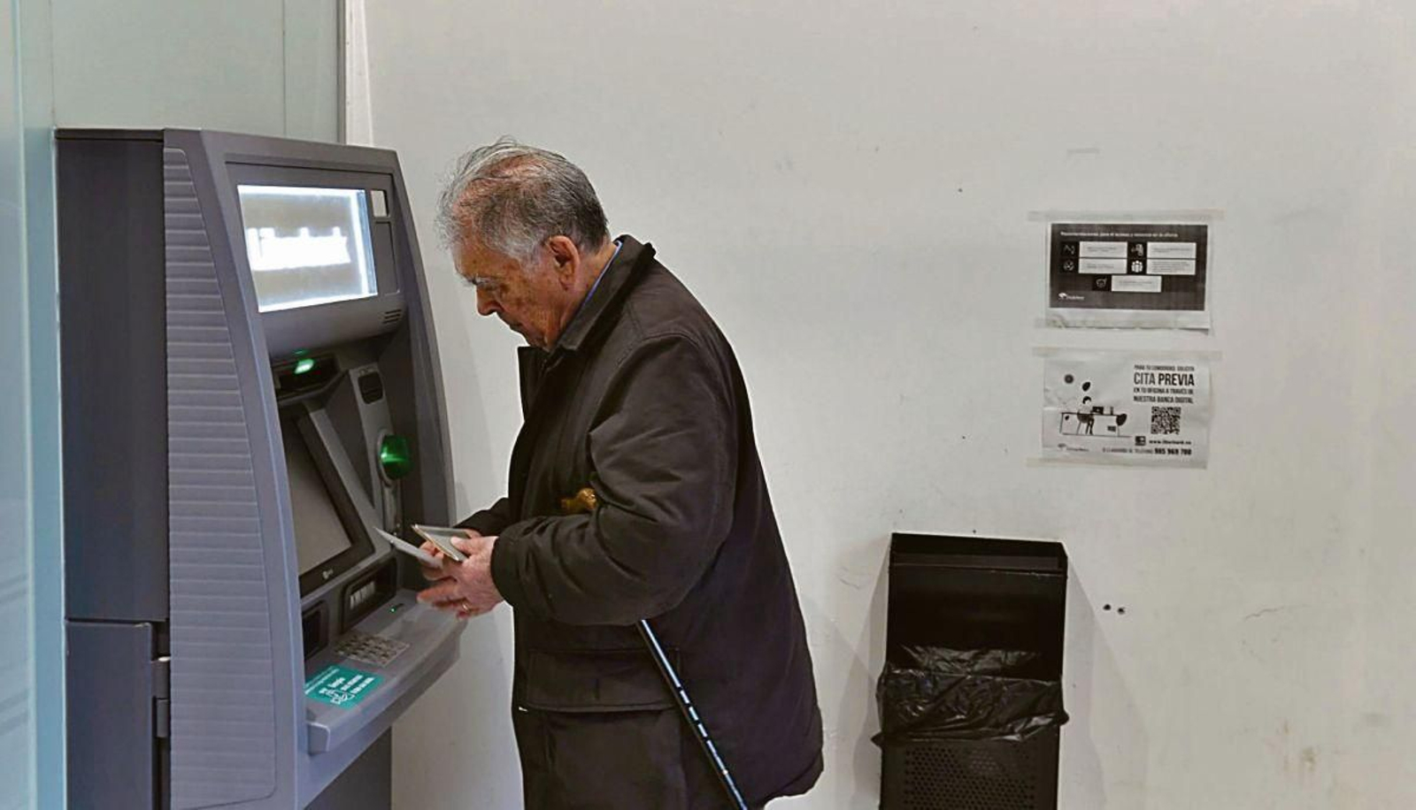 Un hombre de avanzada edad saca dinero de un cajero automático de una entidad bancaria.