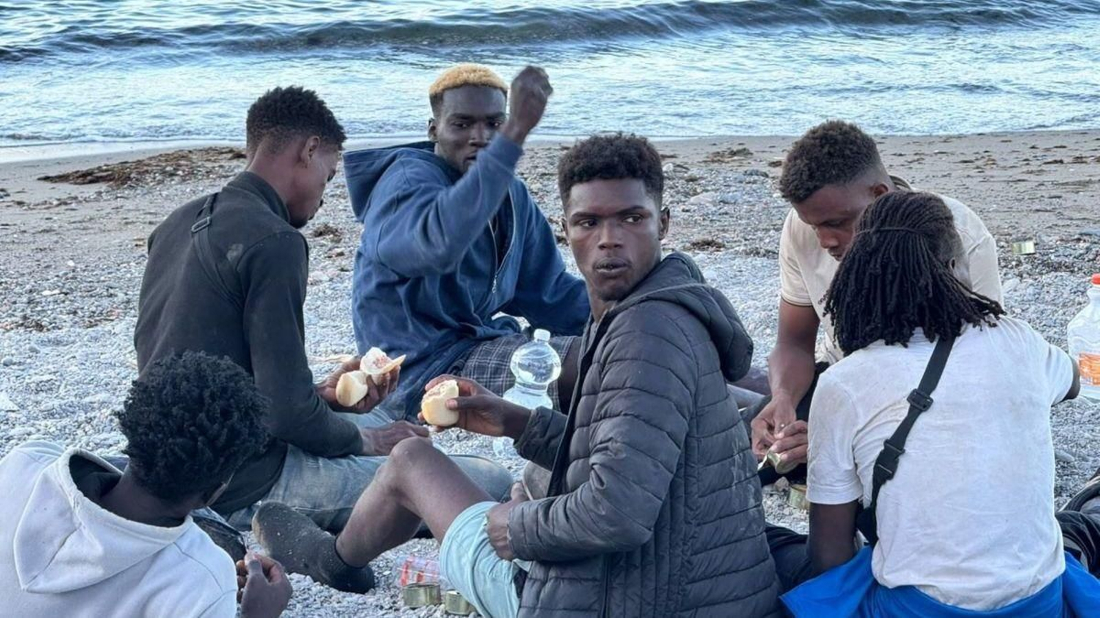Un grupo de migrantes comen en la playa de Trampolín.