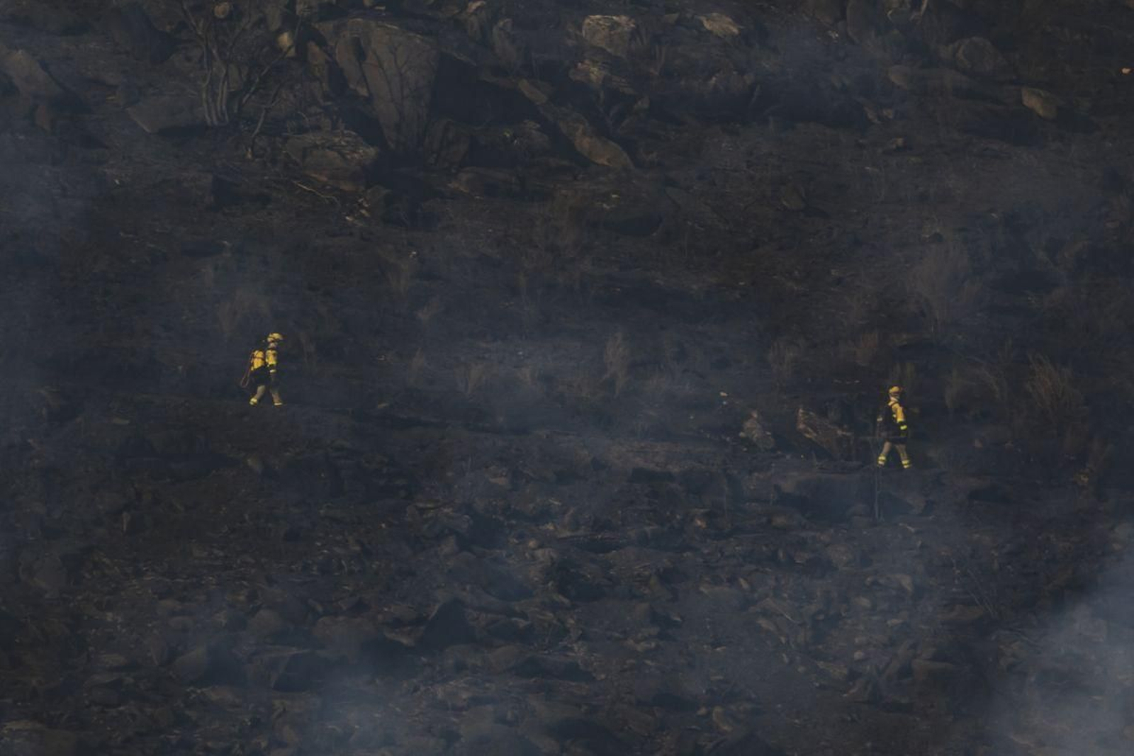 Efectivos caminan por el terreno calcinado por las llamas.