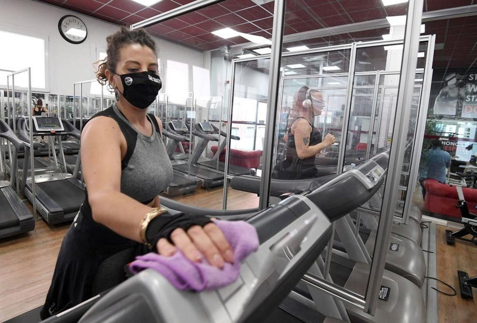 Una de las monitoras de un gimnasio desinfecta una cinta después de su utilización por un cliente.