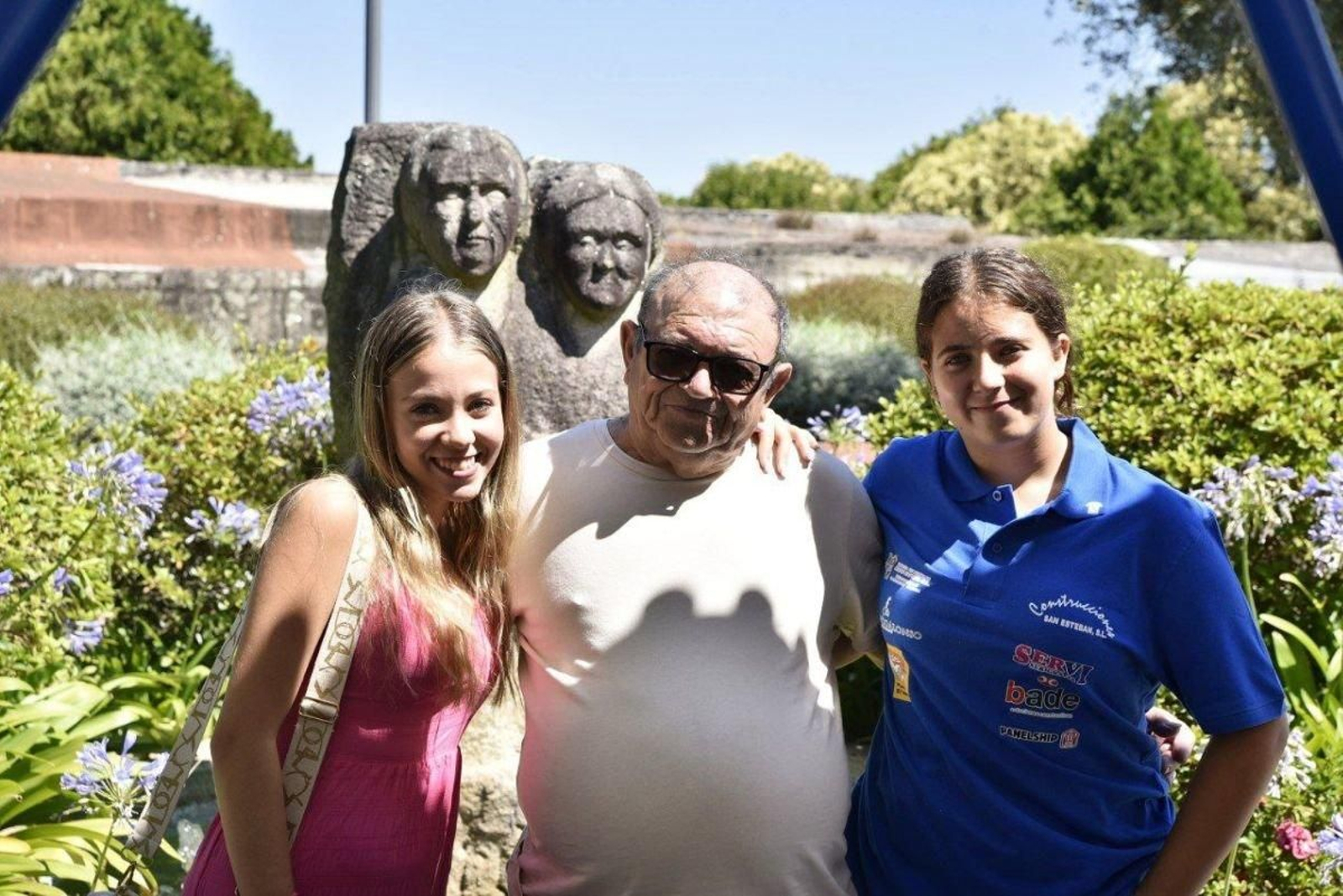 Pepe, un abuelo de Beade, con sus nietas Sara y Antía, junto a la estatua que conmemora a los abuelos en la alameda de la parroquia.