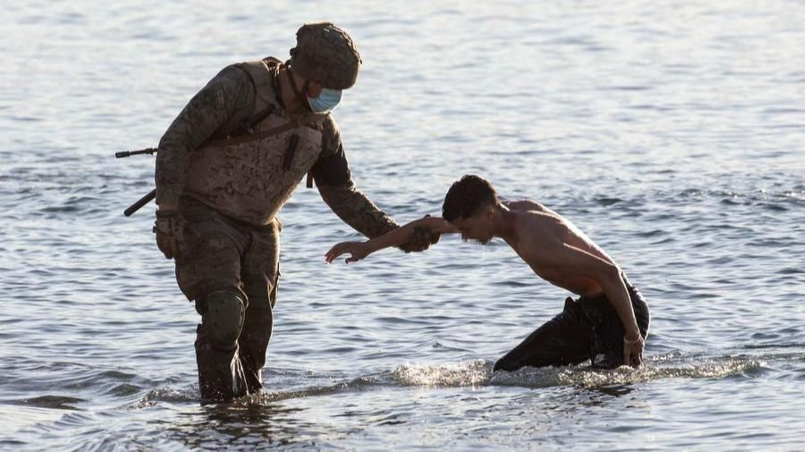 Un militar español ayuda a salir del agua a un joven magrebí en la playa del Tarajal.