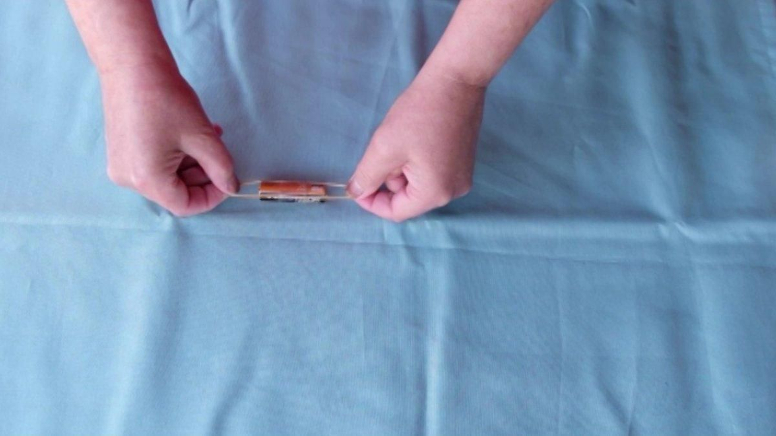 Para que o boneco camiñe ben, tes que prestarlle atención a este paso. Deixamos os vasos a un lado e collemos a pila, a goma e un pouco de celo. Rodea a pila coa goma elástica e aprétaa contra os laterais da pila. Rodea con celo para que quede todo ben fixado como ves na imaxe.