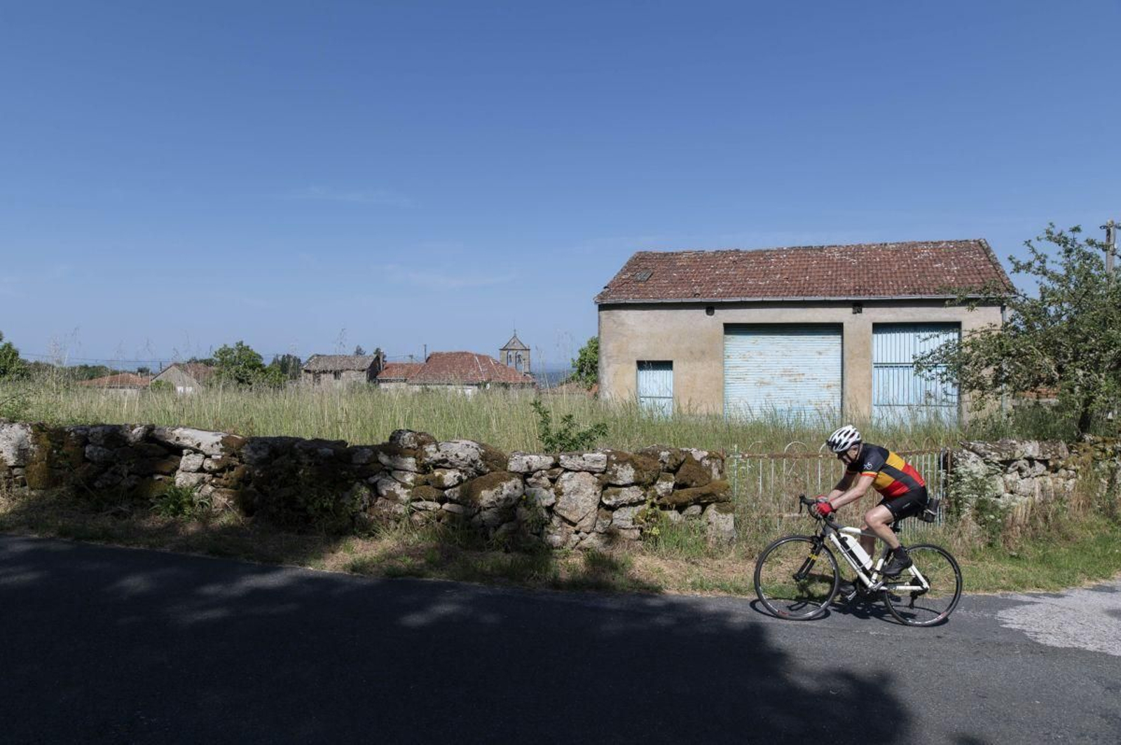Un ciclista pasa junto a una parcela llena de hierba sin desbrozar situada al lado de casas en la aldea de Nogueira, situada en Nogueira de Ramuín