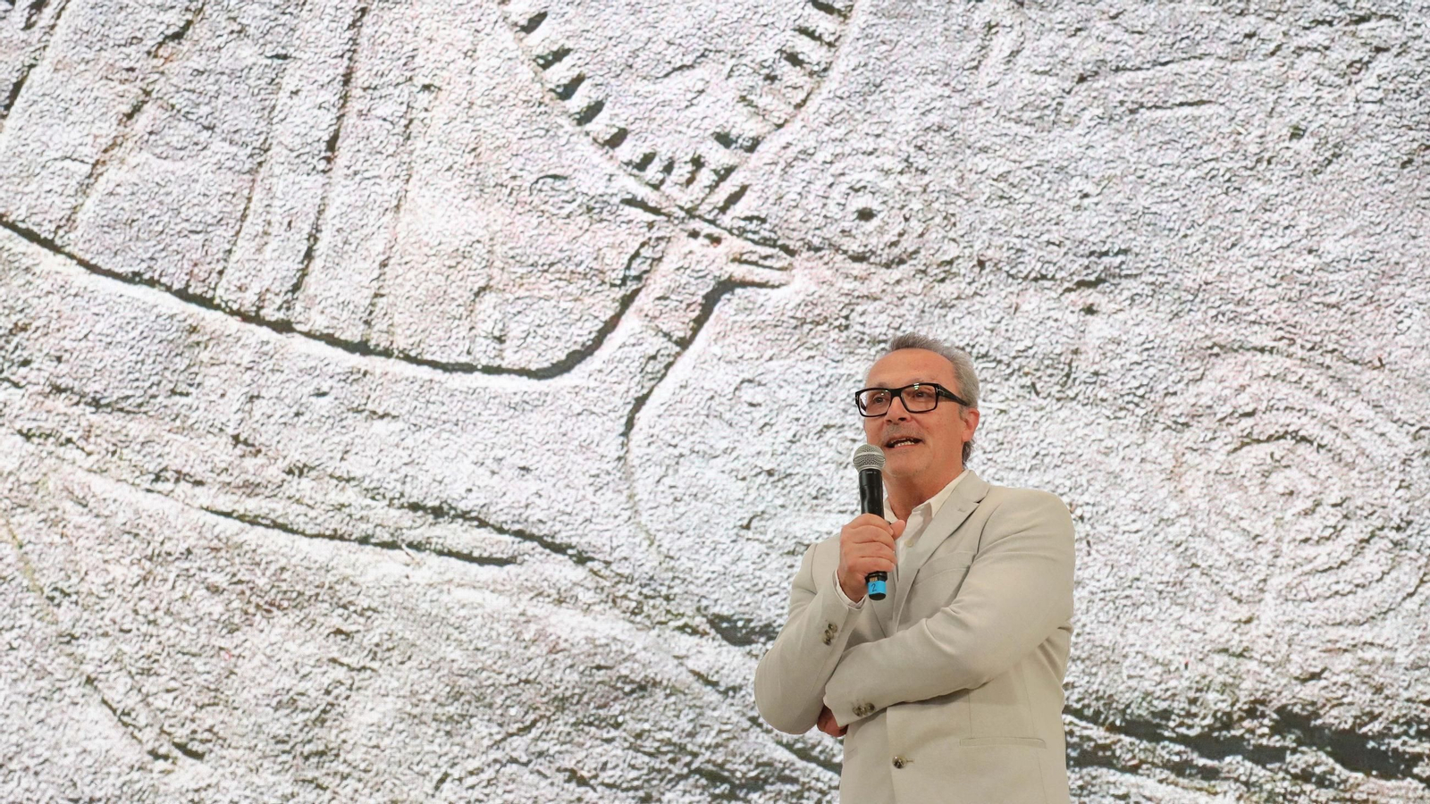 Manuel Santos-Estévez, nunha charla sobre a arte rupestre, cun petroglifo de Campo Lameiro.