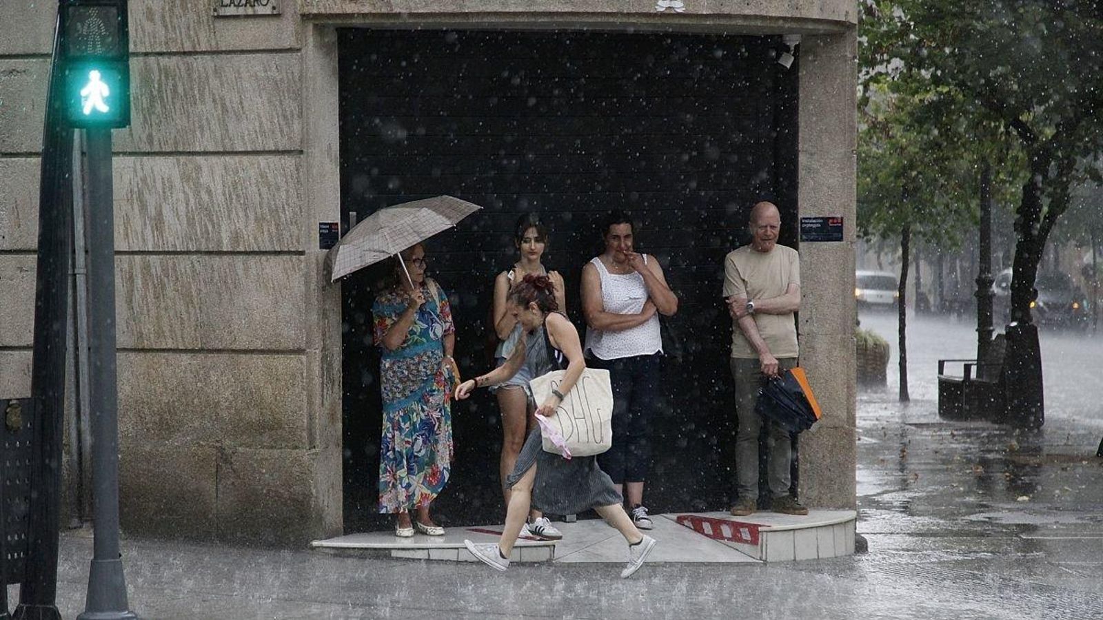 Los vecinos se refugian en el portal de un comercio durante la lluvia, que pilló a algunos desprevenidos.