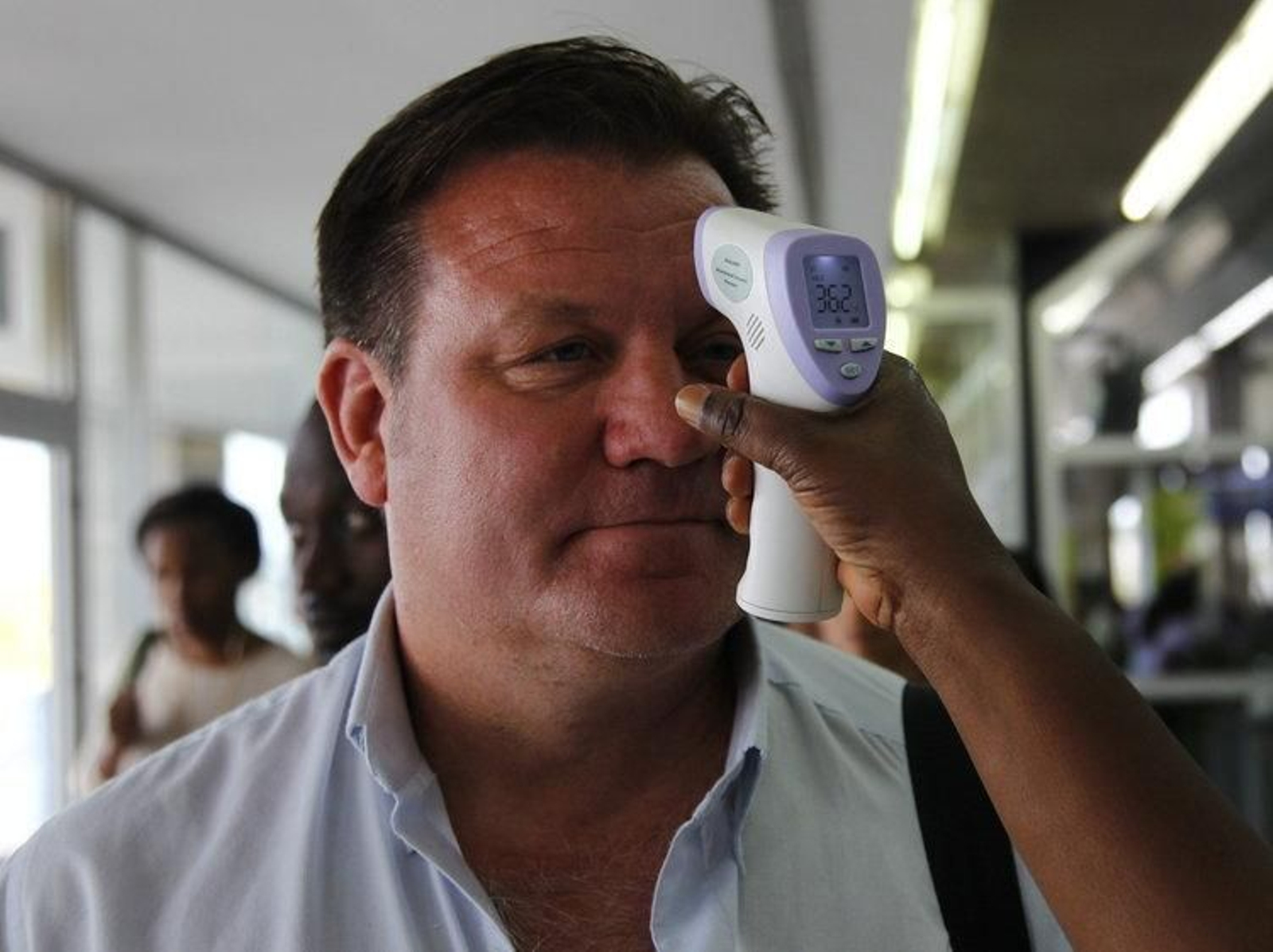 Un miembro del personal del aeropuerto de Abidjan, en Costa de Marfil, mide la temperatura de un turista (KOULA)